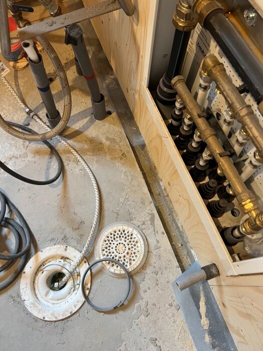 Ingjutna rör och avlopp i ett ofärdigt badrum med isolering och plywood på väggarna, urgröpning synlig i golvets betongyta.