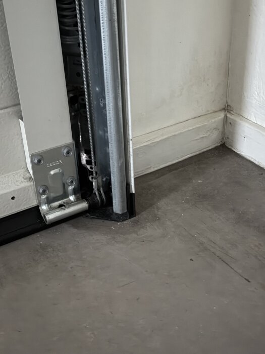 Glapp under garageport med svart tätning och synliga metallbeslag; fuktiga märken syns längs golvet och väggen.