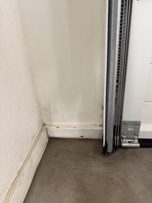 Mögel och fuktfläckar vid garageportens hörn nära golvet.