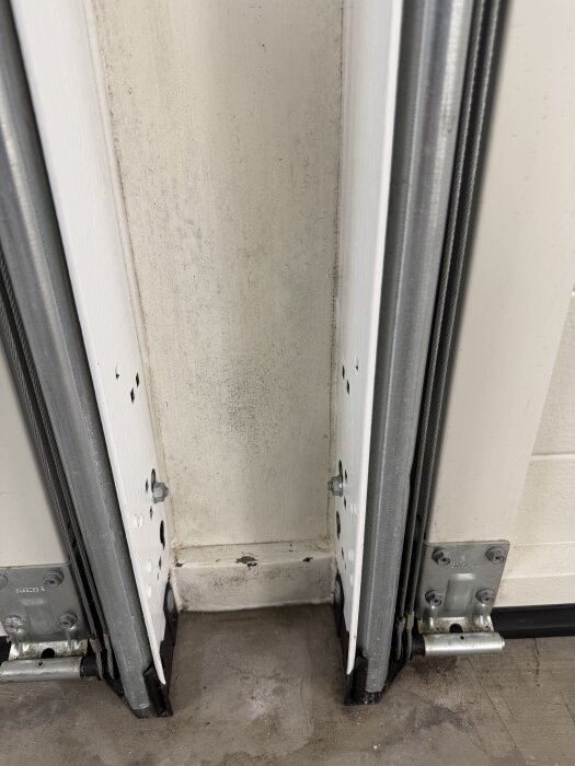 Glapp under garageport med fuktiga golvytor, anslutande till två metallspår, potentiell anledning till mögel bredvid portarna.