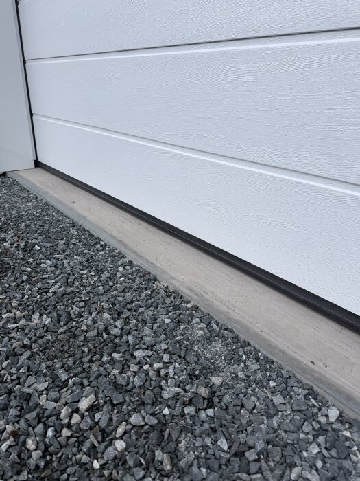 Glapp under garageporten med grus och betong utanför, antyder fuktproblem.