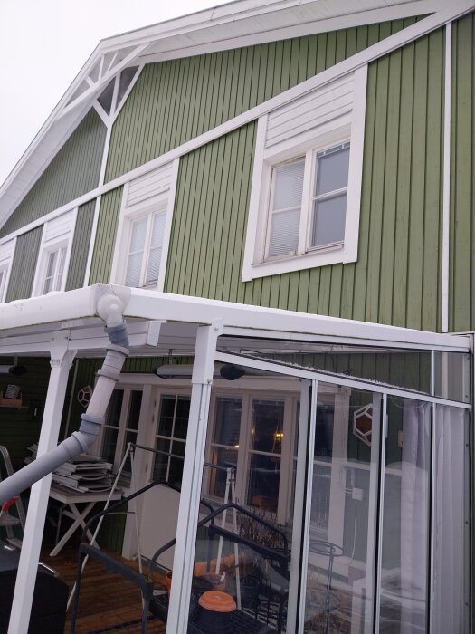 Grönt trähus med vitt kanalplasttak på altanen, synligt stuprör; inlägg handlar om att demontera utan skador.