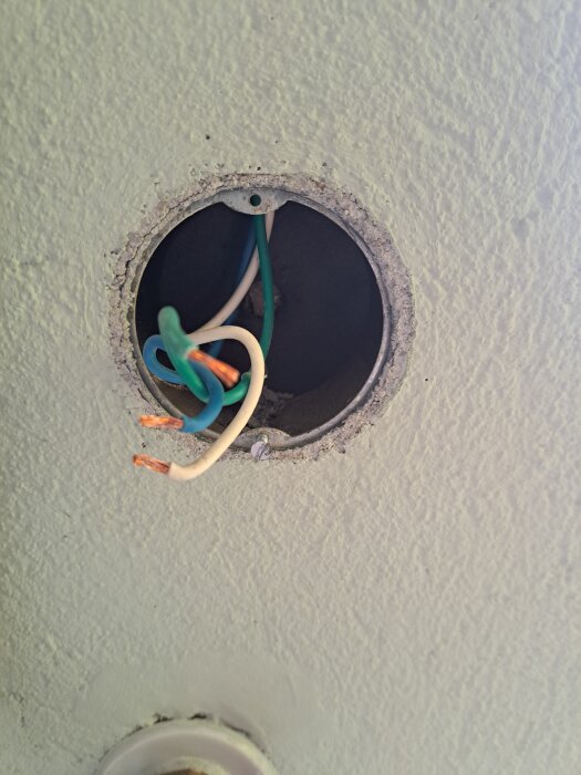 Elektrisk installation i väggen med fyra lösa ledningar: grön, vit, blå och brun, synliga i ett runt hål i betongväggen.