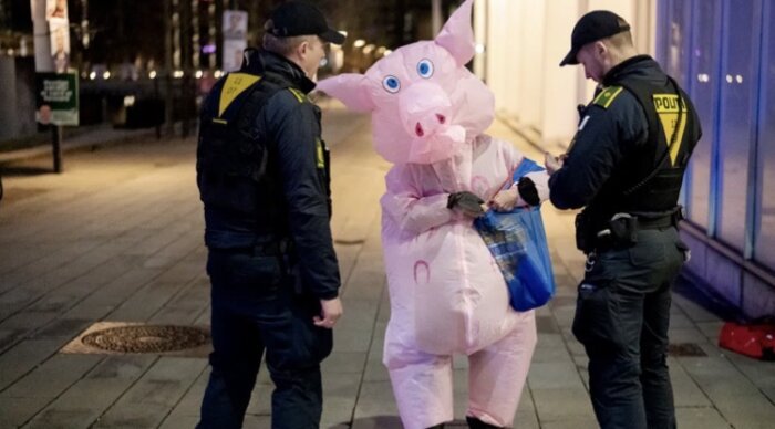 Person i grisdräkt stoppad av två poliser på en trottoar, med en blå påse.