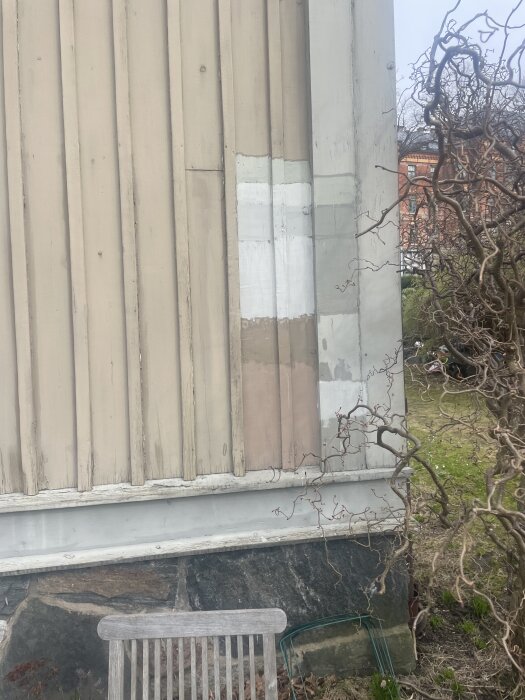Fasadvägg med olika färgprover i vitt och beige, omgiven av träd och buskar.