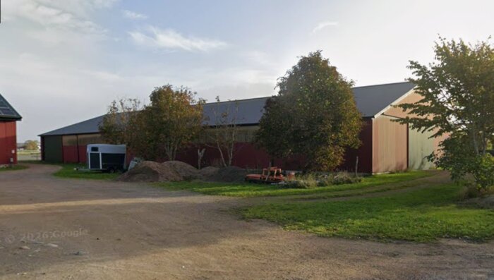Ridhus med plåttak och omgivande träd, fotograferat från marknivå. Det finns en grusväg och en gräsyta framför byggnaden.