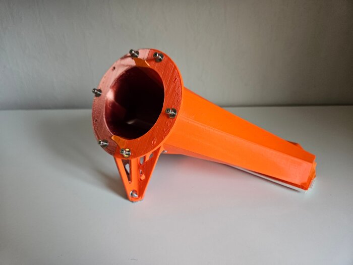 3D-printad orange stos/adapter för luftflödesmätning, gjord i PLA-plast med fästen av flera skruvar, placerad på en vit yta.