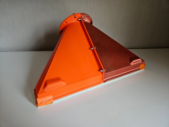 3D-printad stos/adapter i orange och brunt PLA-plast, designad för att mäta luftflöde genom spaltventiler, visas på ett bord.