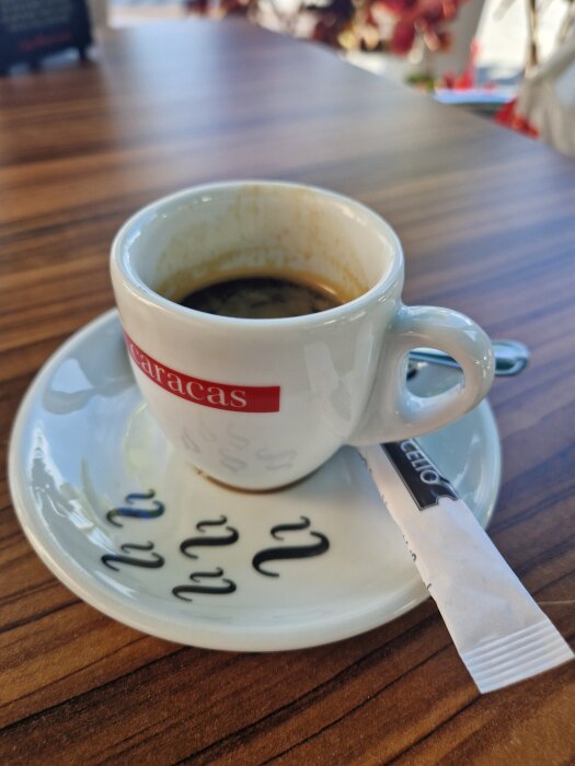 Kopp svart kaffe med espressomärke på en uteservering i San Sebastian, solljus reflekteras i bordytan.