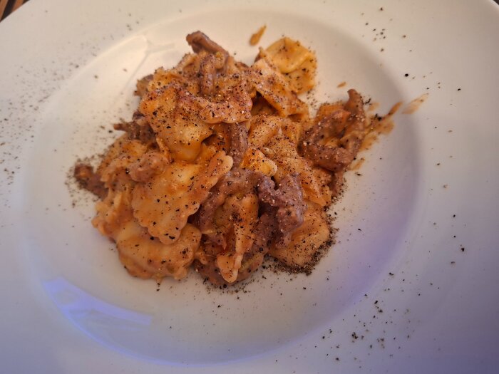 Tortellini med svampfyllning toppad med ragu av strimlad biff och svartpeppar pÄ en vit tallrik.