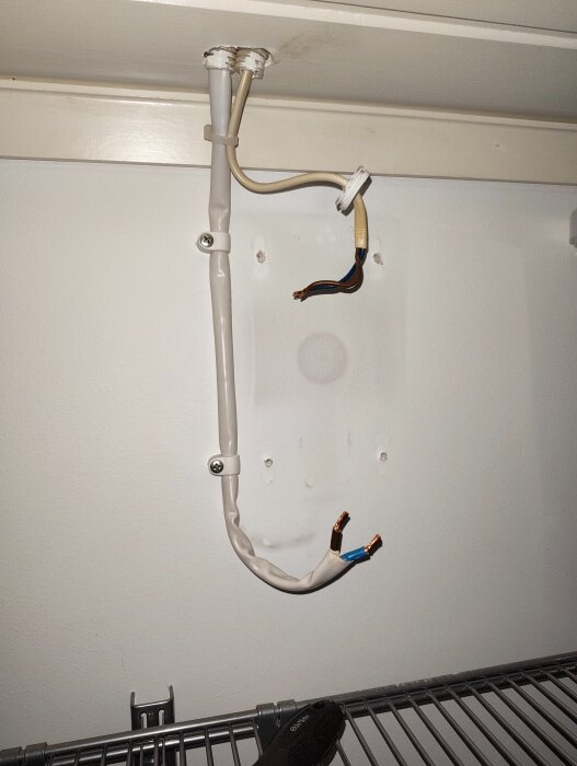 Vit elkabel hänger från taket, exponerade koppartrådar. Kabeln säkert fastsatt med klämmor på väggen, synlig transformatorn har avlägsnats.