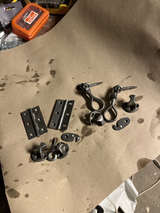 Metallbeslag och gångjärn ligger utspridda på ett bord, förberedda inför fönsterrenovering.