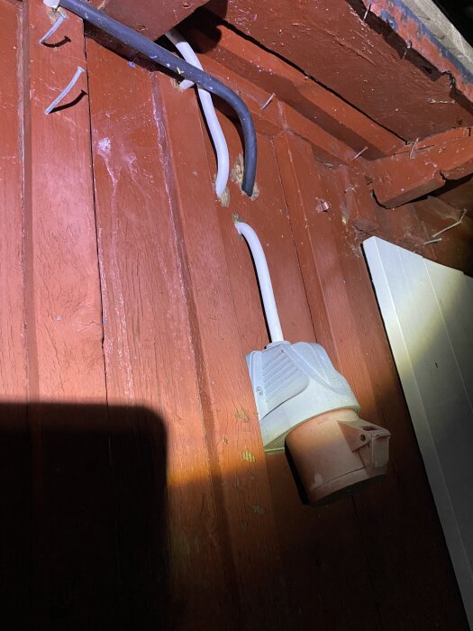 Kabeldragning utanpå röd träpanel med trefasuttag nere till höger.