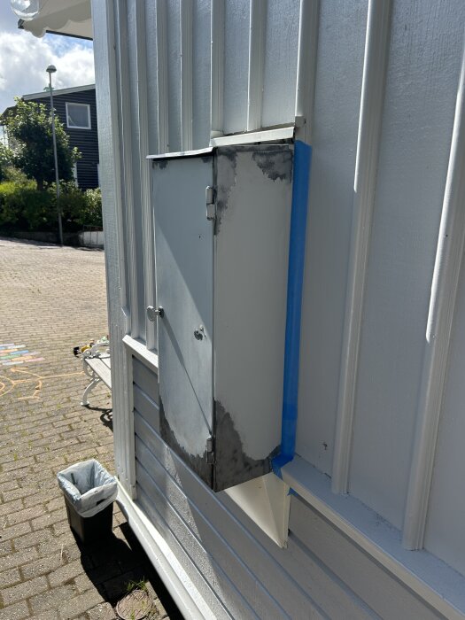 Rostigt elskåp på en husvägg, nymålat med Caparol metalfinish men utan primer, rost börjar synas igen efter slipning och ommålning.