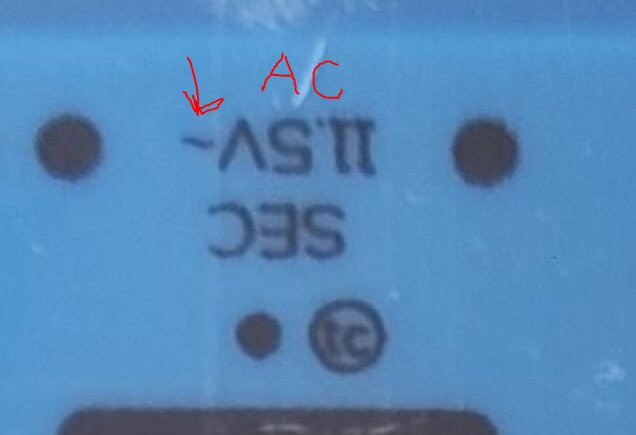 En etikett med texten "SEC" och "11-5V~" markerad med en pil och bokstäverna "AC", antydande växelström på en elektrisk komponent.