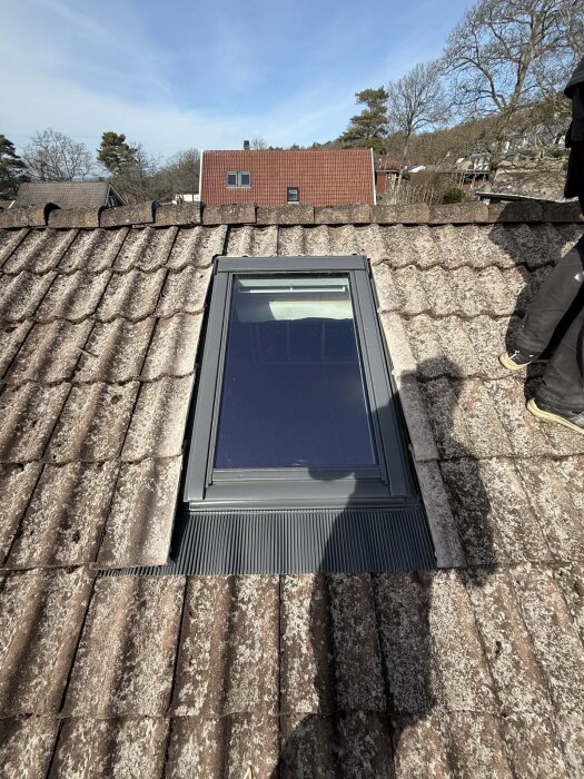 Takfönster installerat på ett tegeltak under en blå himmel, skugga synlig på taket.