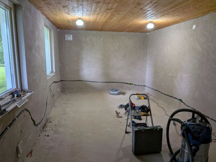 Rum under renovering med sladdar längs väggarna, verktyg placerade på golvet och stege samt dammsugare i förgrunden.