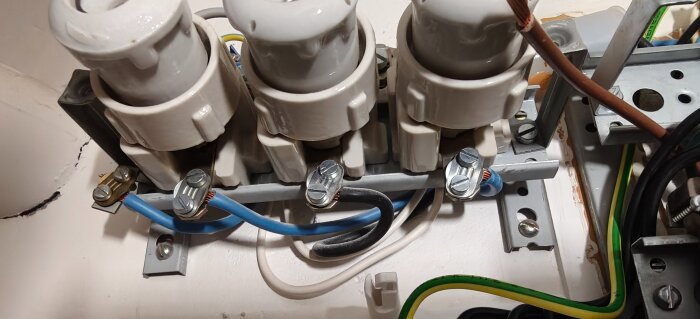 Elektrisk kopplingsdosa med keramiska säkringar och synliga ledningar i blå, svart och grön/gul färg.