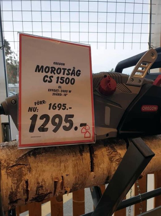Motorsåg modell Oregon CS 1500 med prissänkning från 1695 kr till 1295 kr, visas på stativ över en trästock.