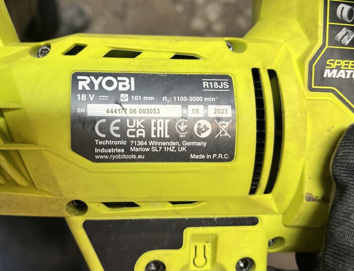 Närbild av en informationsetikett på en gul Ryobi sticksåg R18JS, med tekniska specifikationer och tillverkningsdetaljer.
