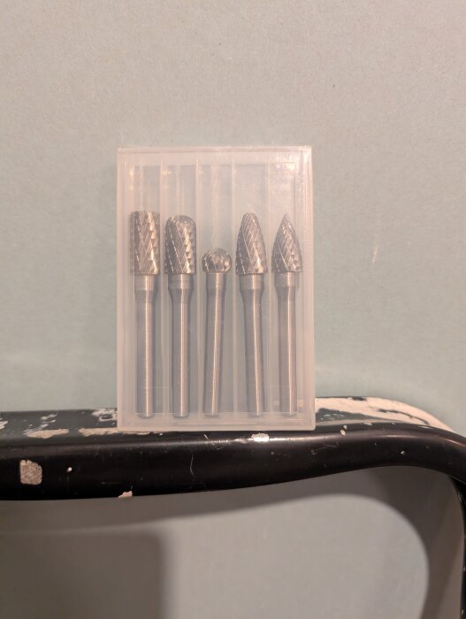 Set med fem olika slipstift i metall för roterande verktyg, förpackade i en transparent plastask, placerad på en svart yta.