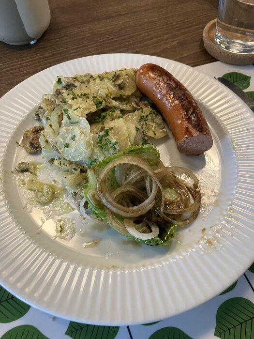 PotatisgratÀng med champinjoner och grÀslök, en chorizo, stekta lökringar och sallad pÄ vit tallrik.
