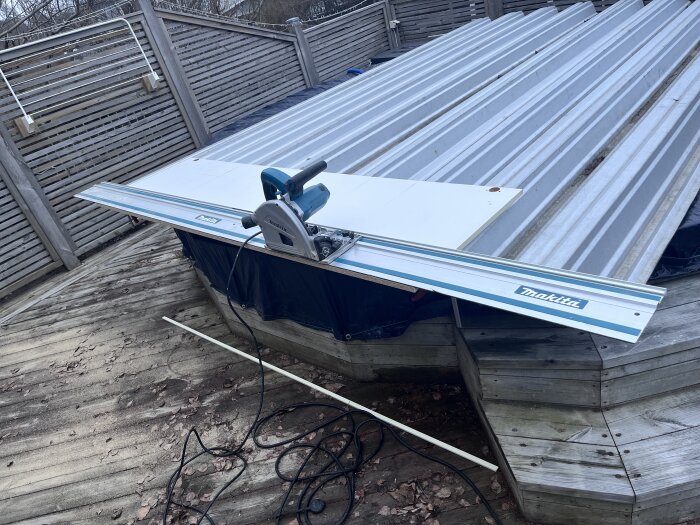 Cirkelsåg på räls från Makita placerad på ett träbord utomhus, med verktyg i bakgrunden och löv på marken.
