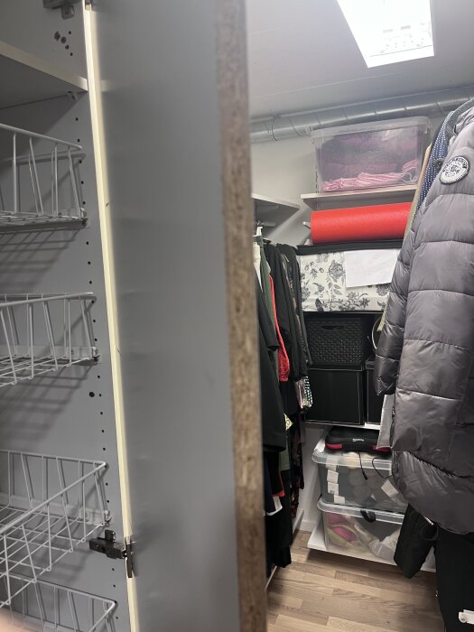 Öppen garderobsdörr i klädkammare, med trådhyllor och kläder, samt plastlådor och röd yogamatta ovanpå en hylla.