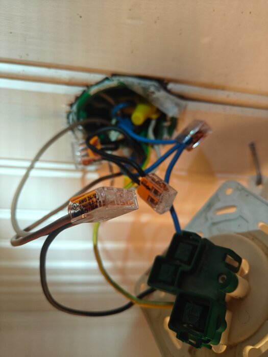 Elinstallation med kablar och kopplingar bakom en strömbrytare, där flera ledningar sammanfogas med kopplingsplintar, ses från sidan.