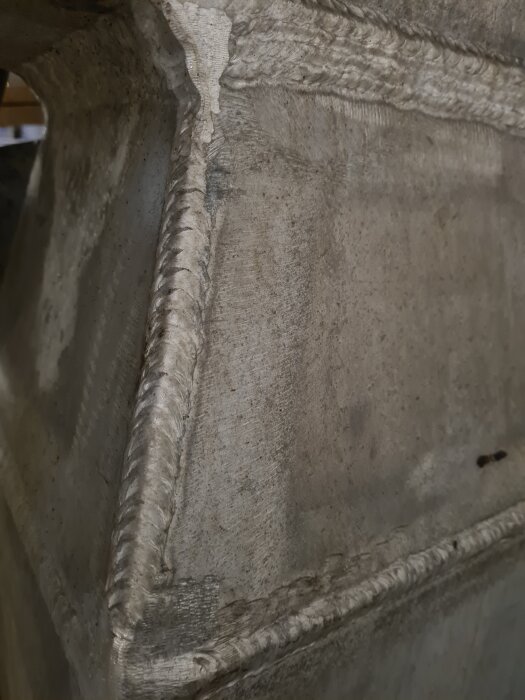 MIG-svetsad aluminiumdel i en större konstruktion, visar svetslinjer och textur på metallen.
