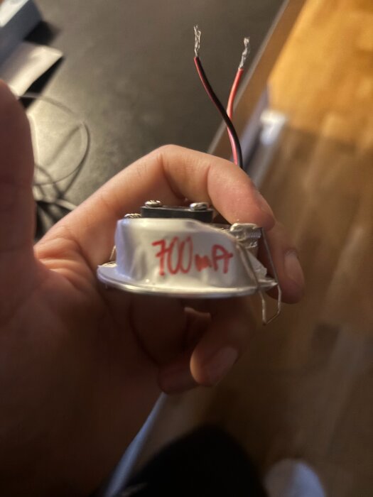 Hand håller i en trasig downlight med två exponerade kablar. Texten "700 mA" är skriven på armaturen.
