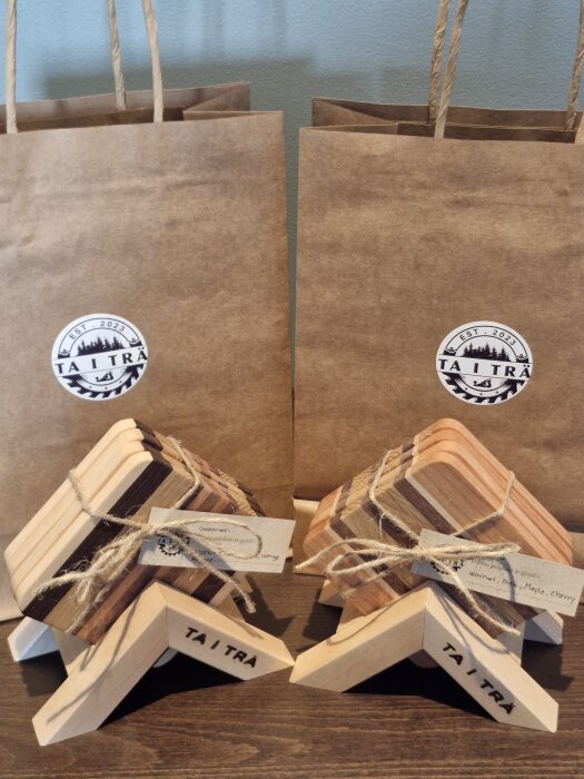 Presentset med ändträskärbräden och coasters i trä, placerade framför två papperspåsar med logotypen "TA I TRÄ".