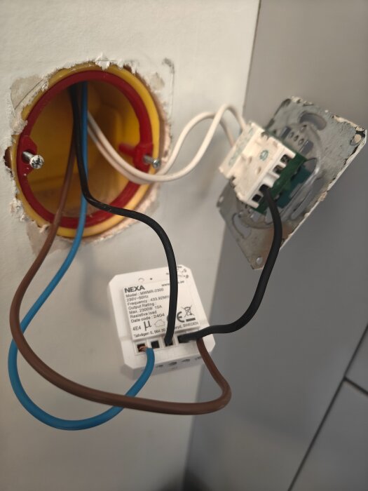Elektrisk kopplingsbox med Nexa-modul och exponerade kablar, inklusive bruna, blåa och svarta, kopplade till en strömbrytarpanel.