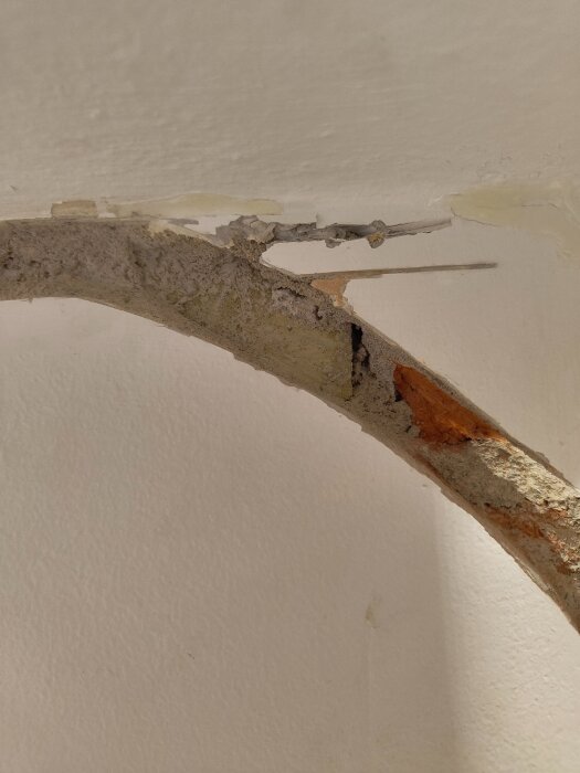 Upptagen ränna i tegelvägg med synlig möjlig eternitfibrer och skador nära radiatorrörens inlopp.