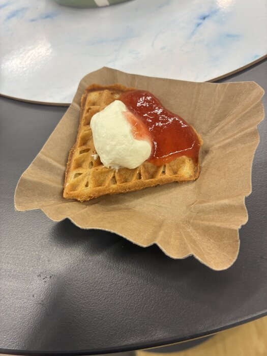 Våffla på papperstallrik med sylt och grädde serverad på ett bord.