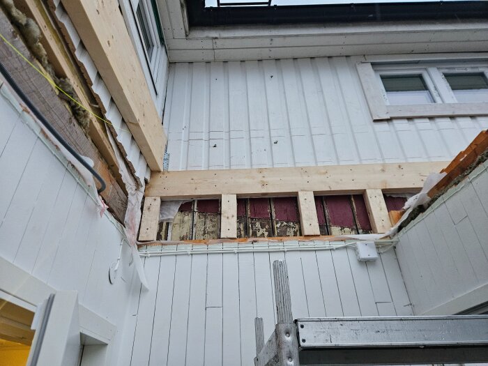 Byggnad under renovering med nya reglar och bärlina i trä, och delar av väggen är exponerade. Träplankor av olika storlekar syns fastsatta.