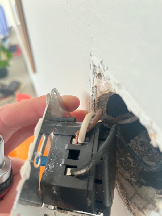 Närbild på en monterad dimmer, med ledningar synliga i väggen och en hand som håller dimmern. En ledning är markerad med ett "x".