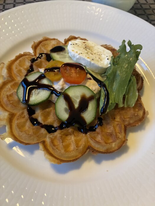 En matvåffla med tonfiskröra, gurka, tomater, sallad och en bit ost, dekorerad med balsamicodressing, serverad på en tallrik.
