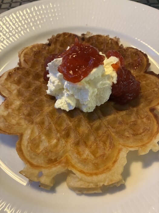En våffla på en tallrik toppad med vispad grädde och jordgubbssylt.