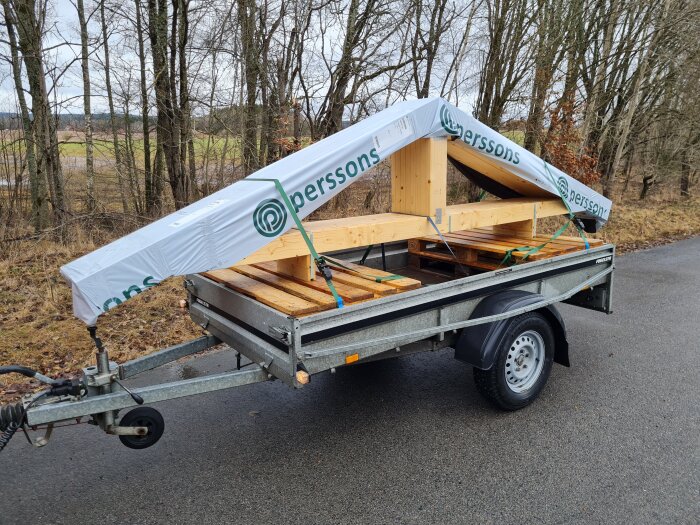 Takstolar på en släpvagn med skog i bakgrunden, redo att användas för en byggprojekt hemma.