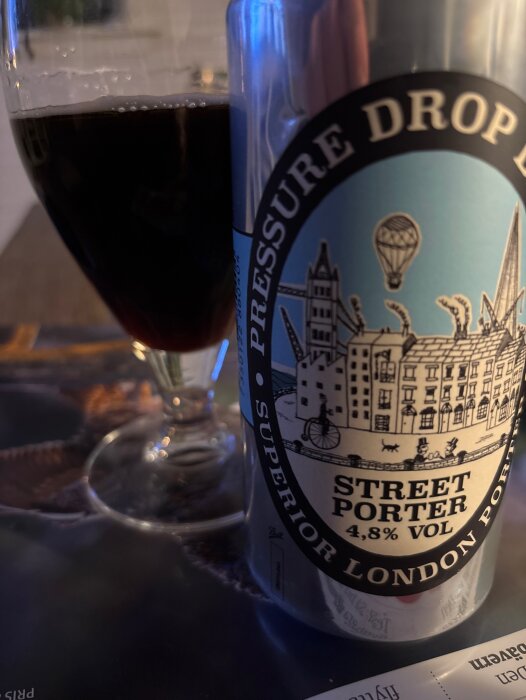 En glas med porter bredvid en burk med etikett "Pressure Drop", märkt "Street Porter 4,8% vol" i kvällsmiljö.