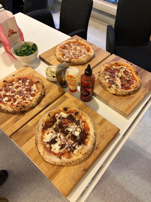 Fyra pizzor på skärbrädor, omgivna av såser och toppings.