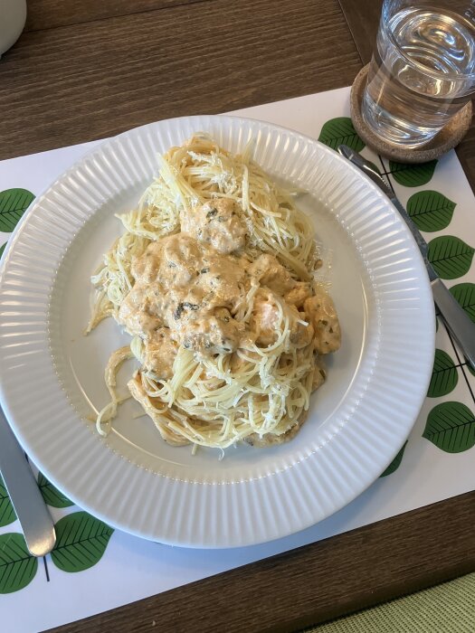Krämig laxpasta med schalottenlök, vitlök, örter och dijonsenap på en vit tallrik, serverad på ett bord.