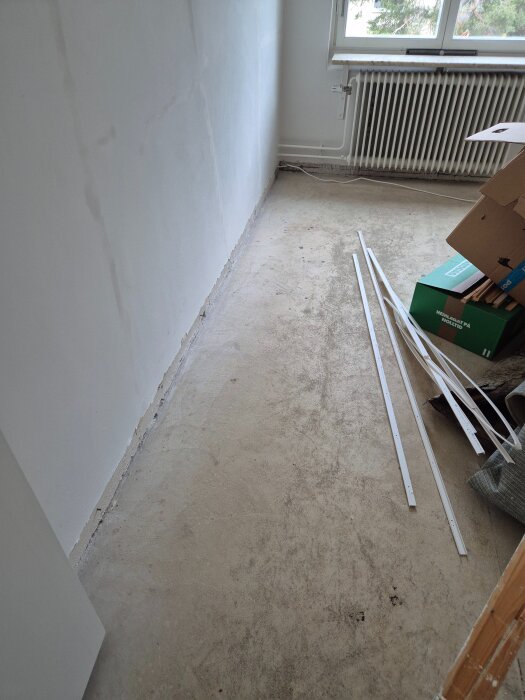 Ett rum med betonggolv där golvlisten är borttagen. Förberett för att lägga nytt trägolv, med byggmaterial och verktyg vid sidan.