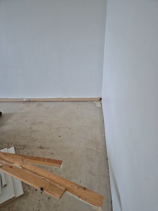 En rumshörna med betonggolv och borttagna golvlister. Trärester och spikar ligger på golvet.