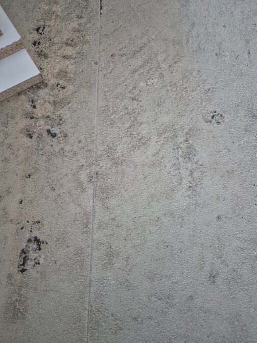 Betongplatta med synliga märken och ojämnheter efter borttagen korkmatta, visar underlaget för planerat trägolv.