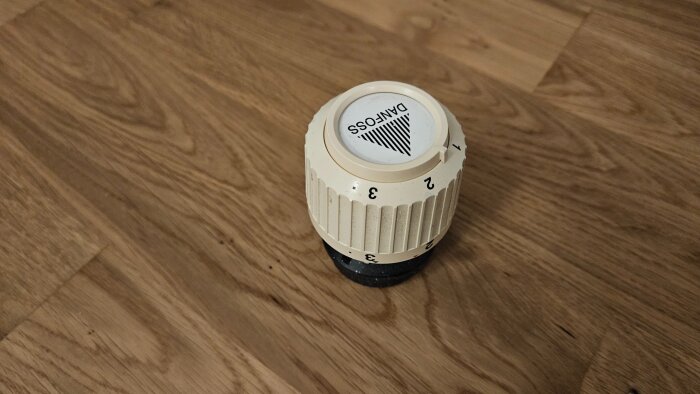 Danfoss radiatorventil i plast på trägolv, märkt med siffrorna 1-3 och med Danfoss logotyp.