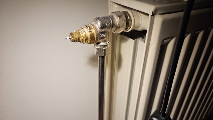 Närbild på en äldre radiatorventil av märket Danfoss monterad på ett element, utan termostat, med ett metallrör anslutet.