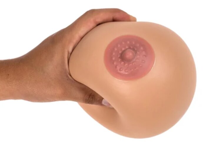 Hand klämmer på en stor stressboll formad som ett bröst, med en rosa del på framsidan.