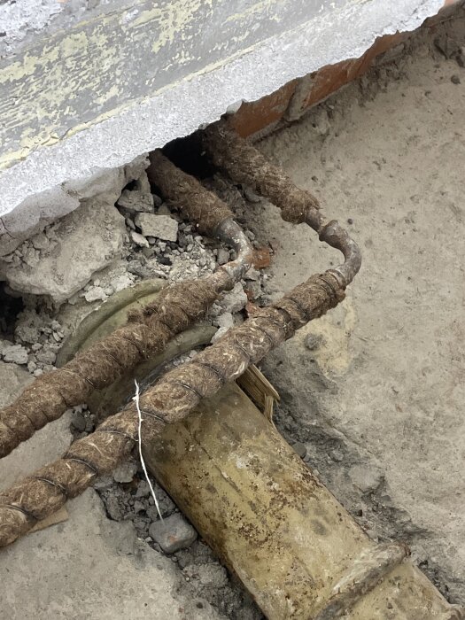 Rör och armeringsjärn i en delvis raserad betongvägg synliga under ett renoveringsprojekt.